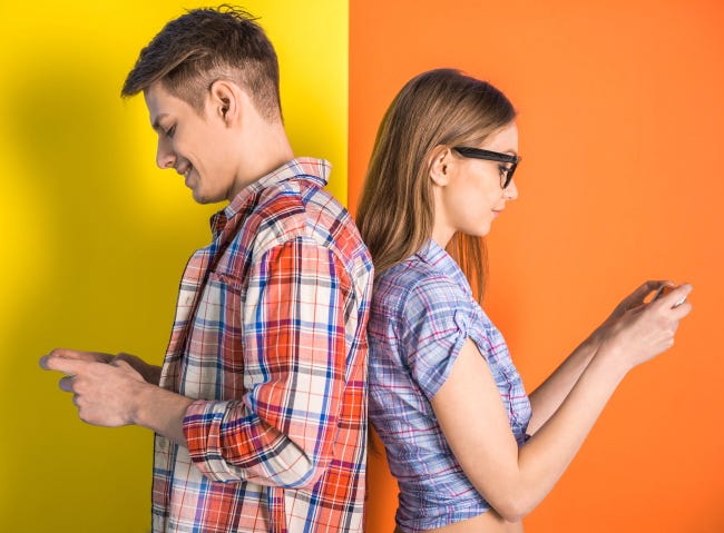 Una pareja joven está de pie espalda con espalda y jugando con un teléfono móvil.