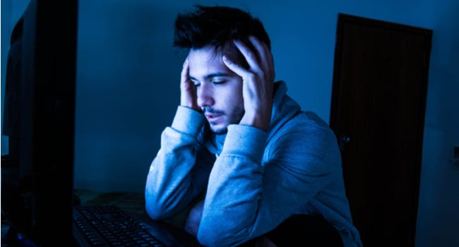 El hombre parece estresado o agotado mientras usa la computadora en la oscuridad.
