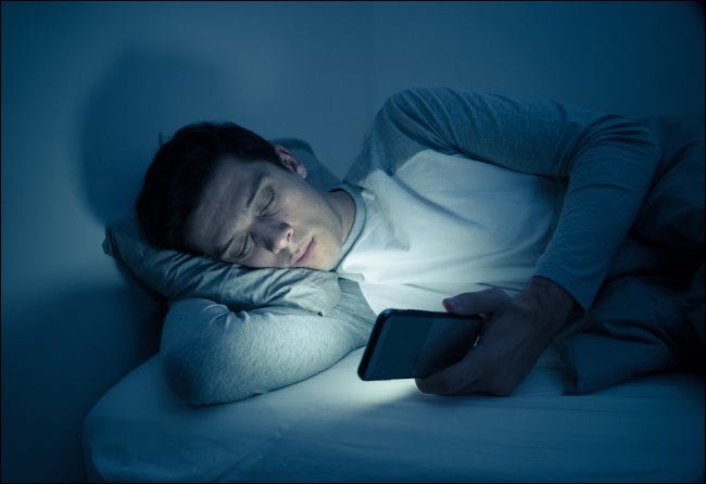 Un hombre envía mensajes de texto en su teléfono inteligente mientras está acostado en la cama por la noche.