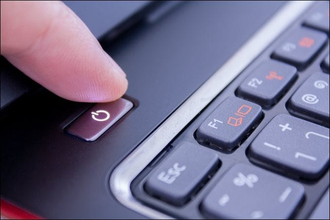 Un dedo presionando el botón de encendido de la computadora portátil PC para apagarlo.