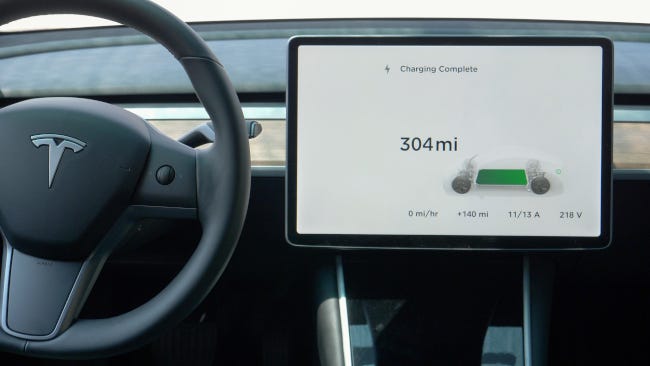 Una pantalla táctil junto al volante de un automóvil Tesla que muestra un mensaje de carga completa.
