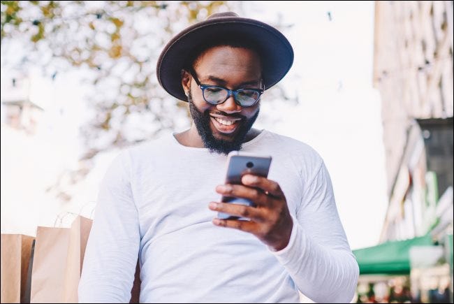 Un hombre sonríe y mira un teléfono inteligente.