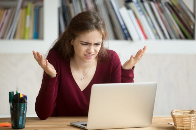 Mujer mirando la computadora portátil con expresión frustrada, manos en el aire